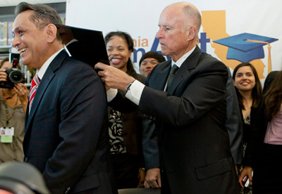 Thống đốc tiểu bang California, ông Jerry Brown (phải), dùng lưng của Dân Biểu Tiểu Bang Gil Cedillo, để ký ban hành đạo luật AB 130 Dream Act tại đại học cộng đồng Los Angeles City College hôm Thứ Hai. (Hình: AP Photo/Damian Dovarganes)